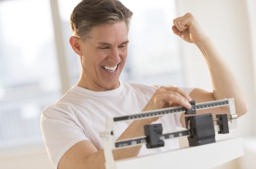 Excited mature man clenching fist while using balance weight scale at gym