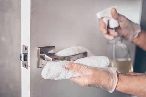 germaphobe cleaning door handle with gloves and sanitizer