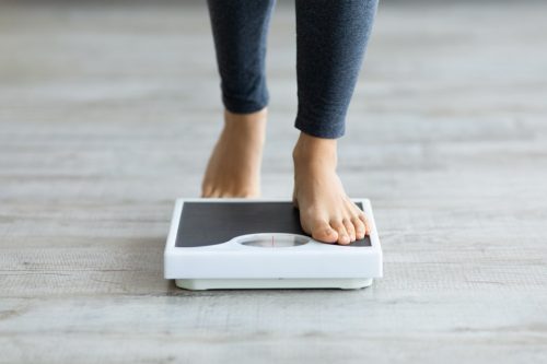 woman stepping on the scale while struggling with a fear of gaining weight