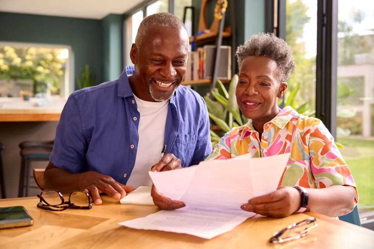 Mature couple smiling and sitting at their kitchen table looking at documents