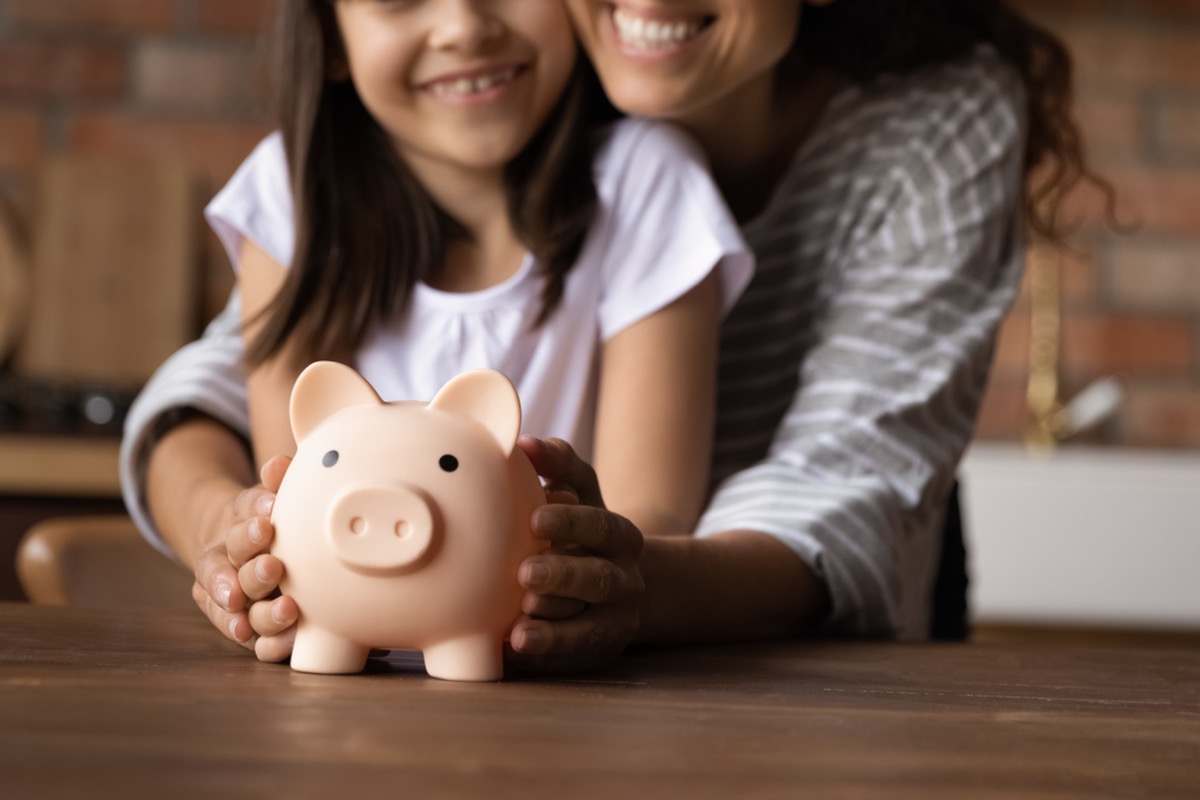Close up happy young mother and adorable little daughter holding touching pink piggy bank, caring mum and adorable girl child saving money for future, family insurance and investment concept