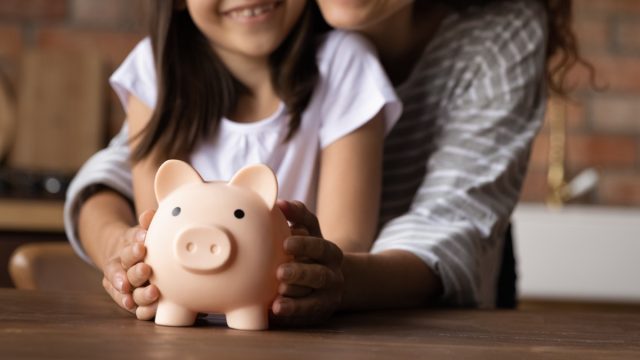 Close up happy young mother and adorable little daughter holding touching pink piggy bank, caring mum and adorable girl child saving money for future, family insurance and investment concept