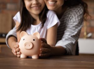 Close up happy young mother and adorable little daughter holding touching pink piggy bank, caring mum and adorable girl child saving money for future, family insurance and investment concept