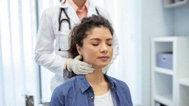 Endocrinologist examining throat of young woman in clinic. Women with thyroid gland test . Endocrinology, hormones and treatment. Inflammation of the sore throat