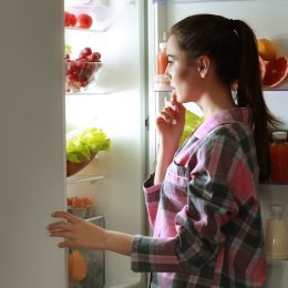Young beautiful woman looking into fridge at night