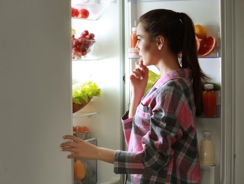 Mujer joven mirando al frigorífico por la noche