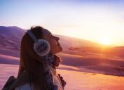 Image of pretty woman walking in snowy mountains, side view of cute girl looking up, closeup portrait of female wearing warm winter earmuff, red sunset, wintertime sports, trekking and hiking concept