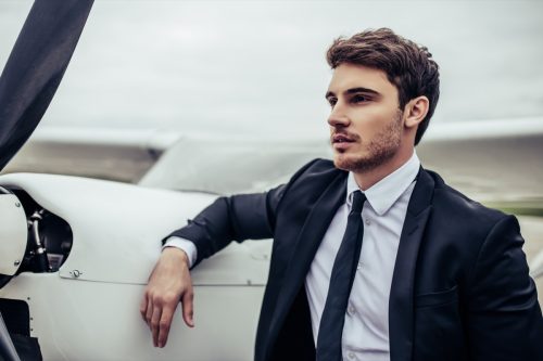 Young man in a suit leaning against a small airplane