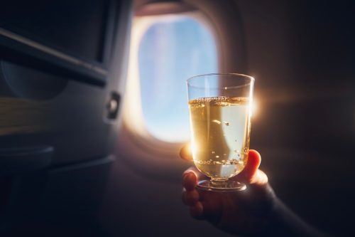 Man enjoying drink during flight. Passenger holding glass of sparkling wine against airplane window.