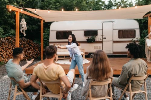 group of friends playing charades outside of a camping trailer