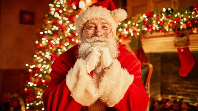 santa claus sitting in front of the christmas tree smiling