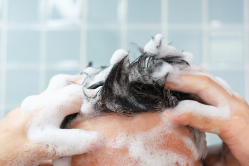 Male hands wash their hair with shampoo and foam on a blue background, front view.