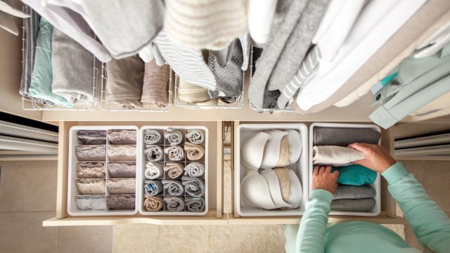 Unidentified neat housewife puts container with socks and pantyhose on wardrobe drawer during general cleaning by modern storage system. Concept of beautiful and comfortable organization