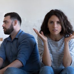Annoyed married couple sitting on couch apart, after conflict, arguing, row. Serious angry wife looking at camera, tired husband turning away. Marriage crisis, counseling, relationships concept