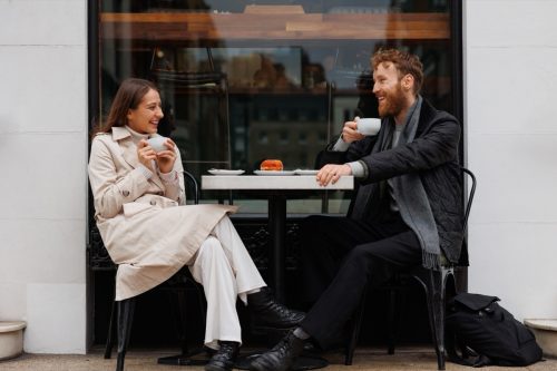 man asking woman questions while seated outside at a cafe