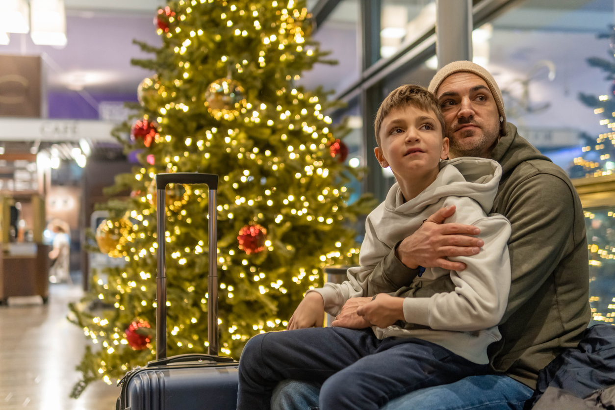 A father and son sitting next to a Christmas tree in an airport terminal waiting for a flight
