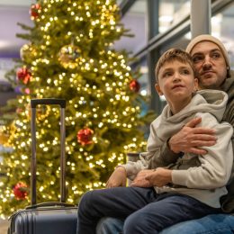 A father and son sitting next to a Christmas tree in an airport terminal waiting for a flight