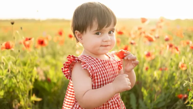 little girl in a red dress holding a flower in front of a field of poppies
