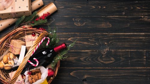 Bottle of red wine and snacks in Christmas basket on wooden table