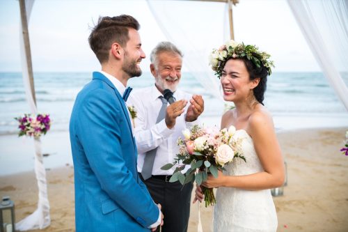 Bride and groom standing in front of officiant on a beach