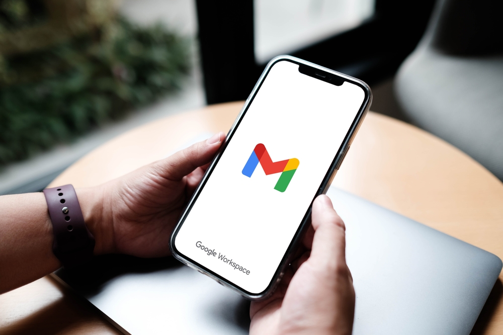 A close up of a hand holding a phone with the Gmail logo on the screen