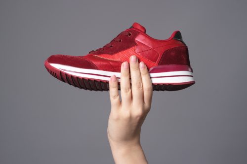 Hand holding new red sport sneaker isolated on gray background.