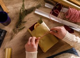 Directly above shot of unrecognizable creative young man wrapping and tying a decorative red and white twine around a cute rustic Christmas gift box that he is decorating.