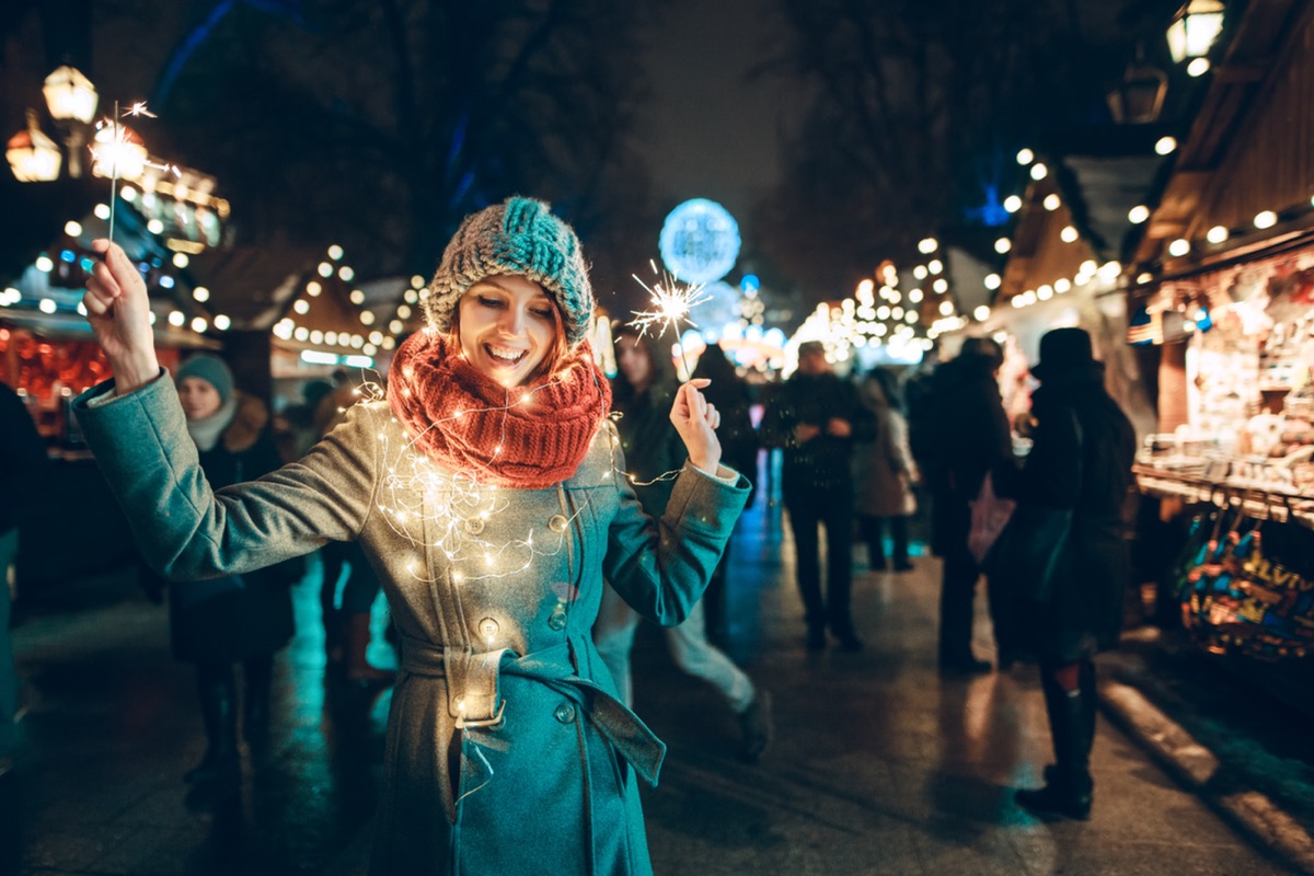 Woman holding sparklers and covered in holiday lights at Christmas market