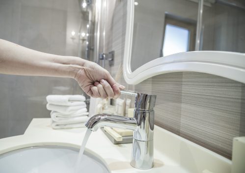 Close-up of woman's hand turning on hotel sink