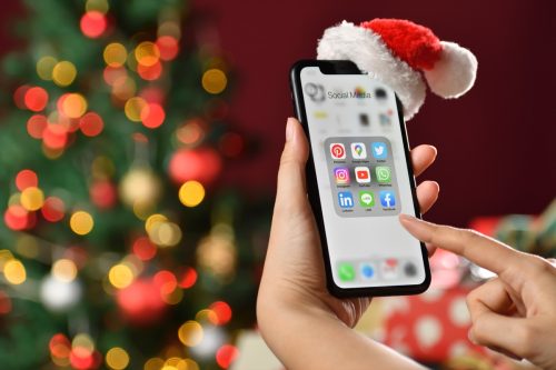 woman holding a smartphone with icons of social media on the screen in front of a christmas tree