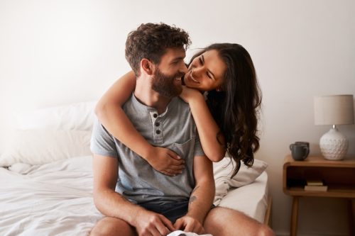 man and woman hugging while sitting on the edge of the bed