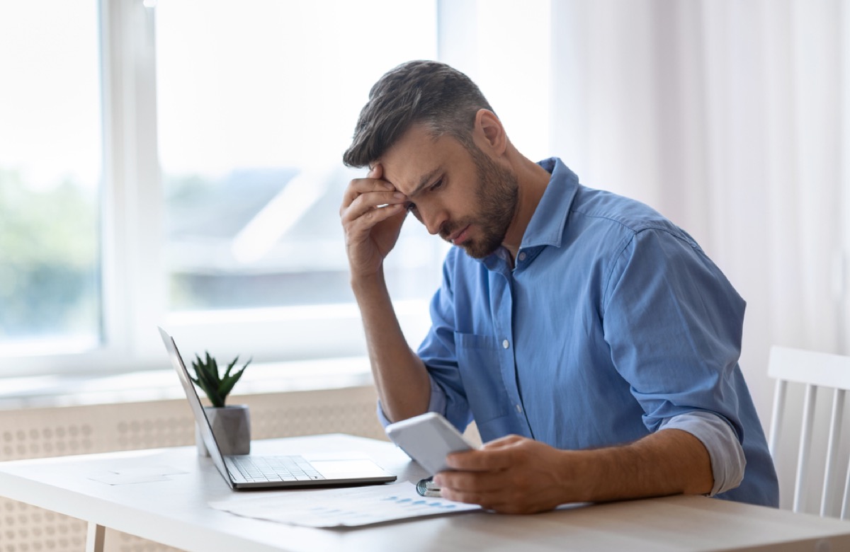 man at desk looking at phone with a worried expression