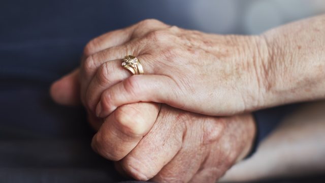 An elderly married couple's hands, clasped tightly in affection.
