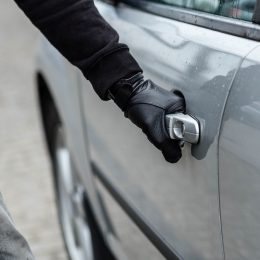 Close up of a thief wearing a black glove breaking into a silver car