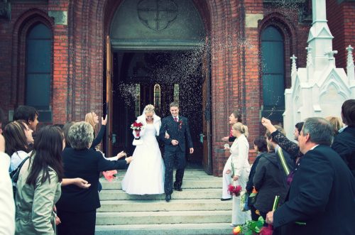 bride and groom at church door with rice confetti being thrown by guests