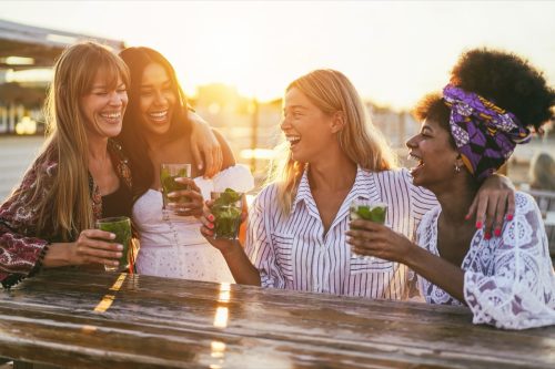 group of young women drinking cocktails at a picnic table during sunset