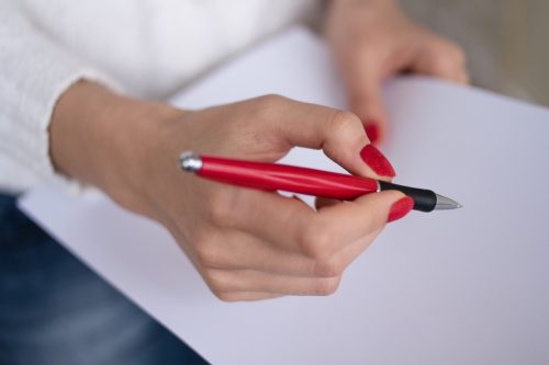 Female hands with red nails write on a sheet of paper