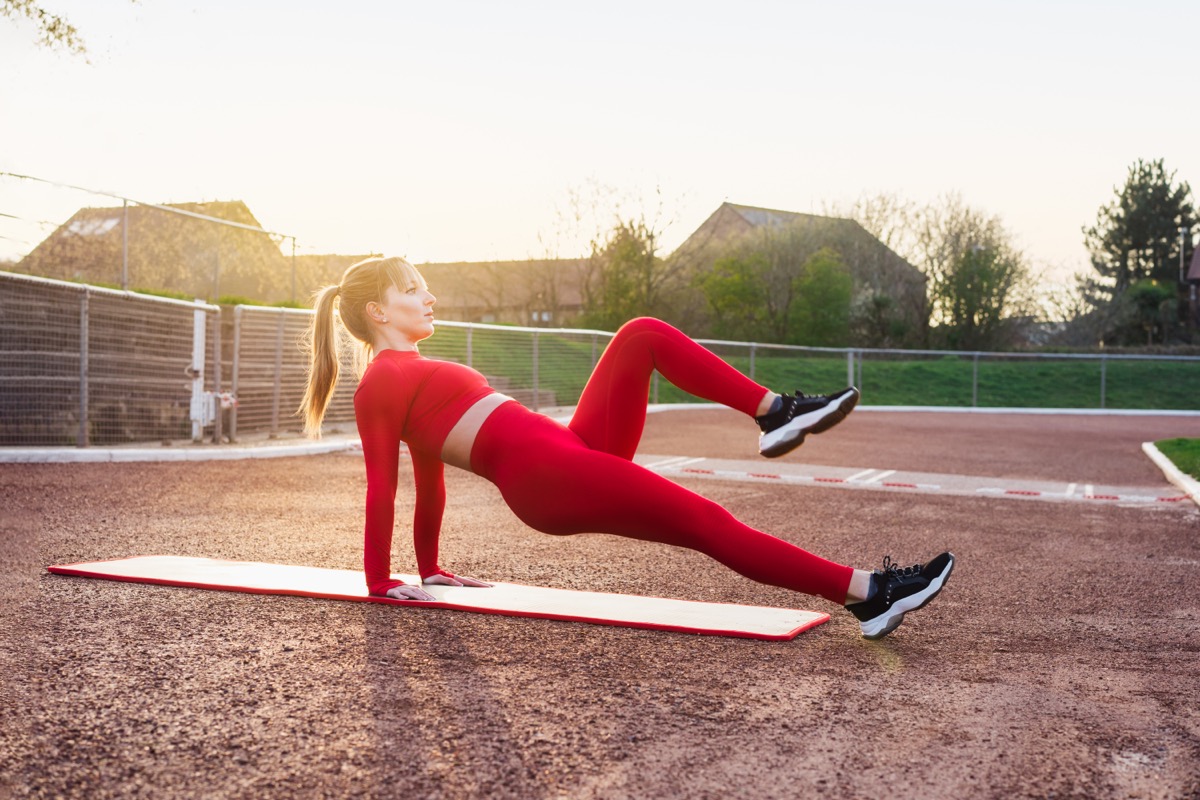 Young fitness woman in red sportswear doing reverse plank knee tuck exercise on a mat