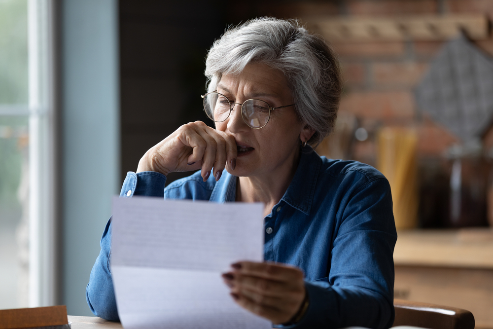 A senior woman reading a letter with a distressed look on her face