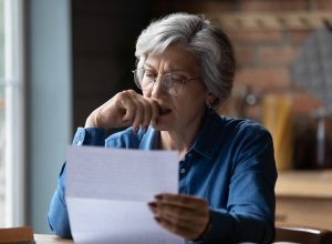 A senior woman reading a letter with a distressed look on her face