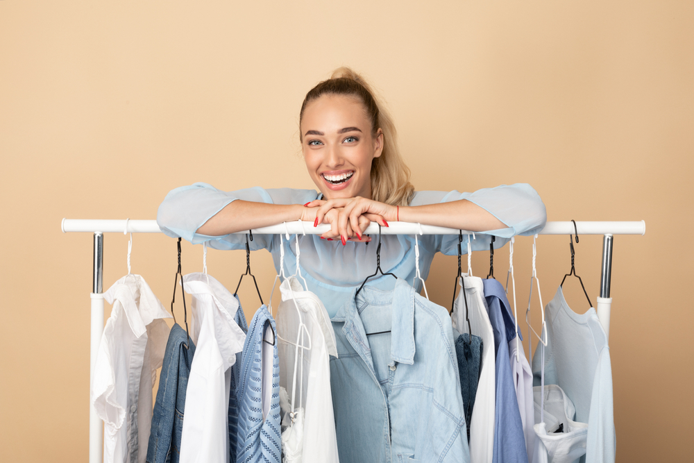 Stylist woman leaning on clothing rack with capsule wardrobe