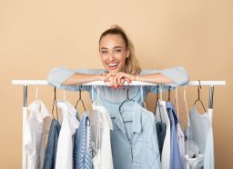 Stylist woman leaning on clothing rack with capsule wardrobe