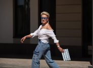 Stylish older woman running through the city in cargo jean pants with clutch and sunglasses