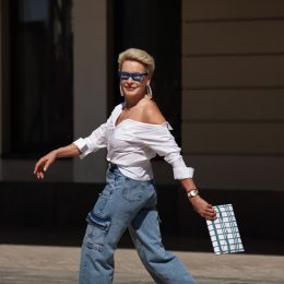 Stylish older woman running through the city in cargo jean pants with clutch and sunglasses