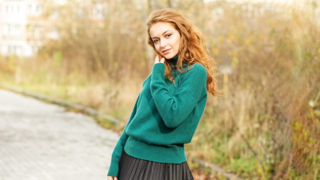 Beautiful red-haired woman in a pleated skirt and a green sweater. Fashion and style concept