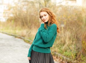 Beautiful red-haired woman in a pleated skirt and a green sweater. Fashion and style concept
