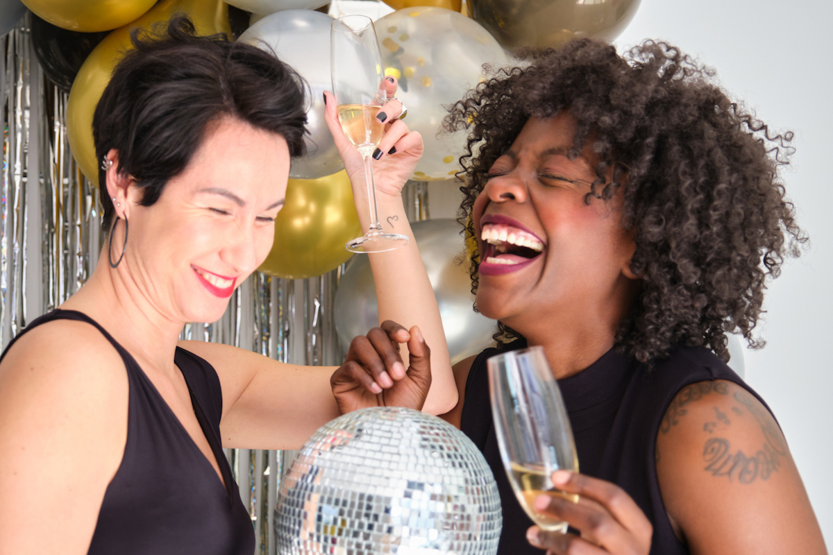 Two women with champagne glasses and disco ball laughing celebrating New Year in a New Years Eve party.