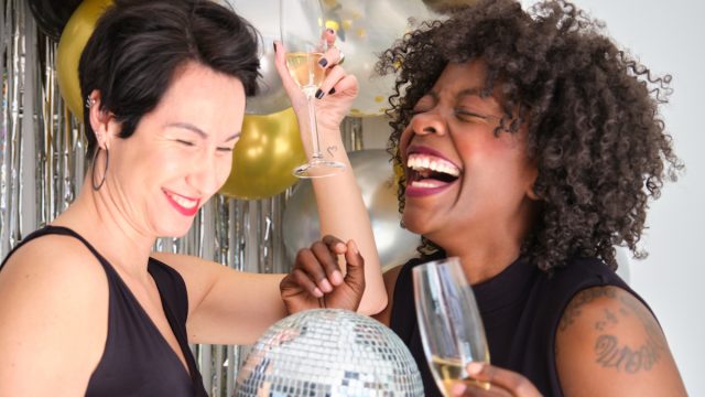 Two women with champagne glasses and disco ball laughing celebrating New Year in a New Years Eve party.