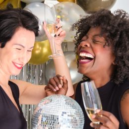 Two women with champagne glasses and disco ball laughing celebrating New Year in a New Years Eve party.