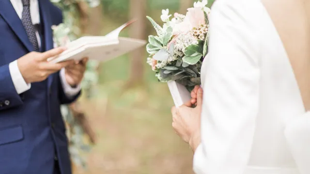 Bride and groom reading wedding vows from paper at wedding ceremony in nature.